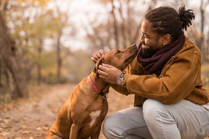 Mann kneler på en skogssti, smiler og klapper en hund med halsbånd mens de berører nesen