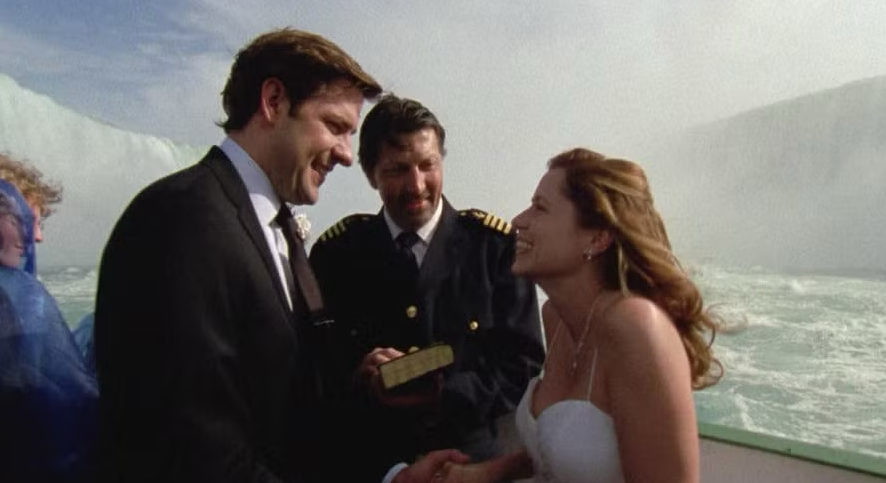 Et par i bryllupsantrekk står på en båt i nærheten av fossefall, og utveksler løfter med en kaptein som funksjonær
