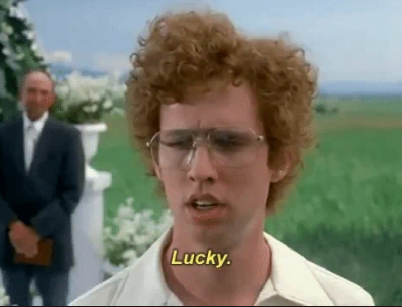 En scene fra en film med en person med krøllete hår og briller som sier & quot; heldig. & Quot; En mann i en drakt står i bakgrunnen