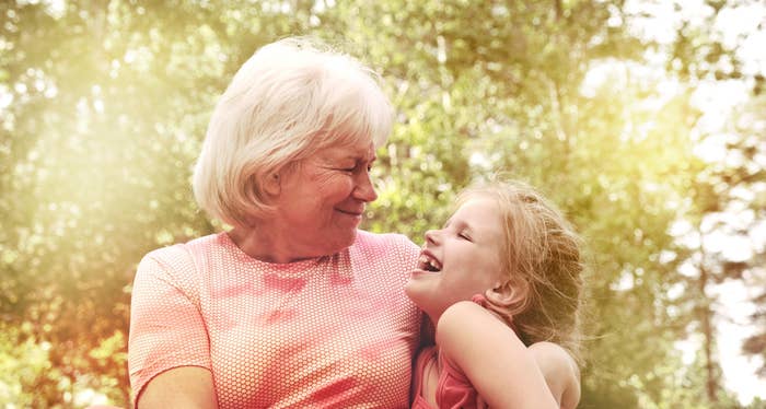 Eldre kvinne og ung jente som smiler til hverandre utendørs, og deler et gledelig øyeblikk omgitt av trær