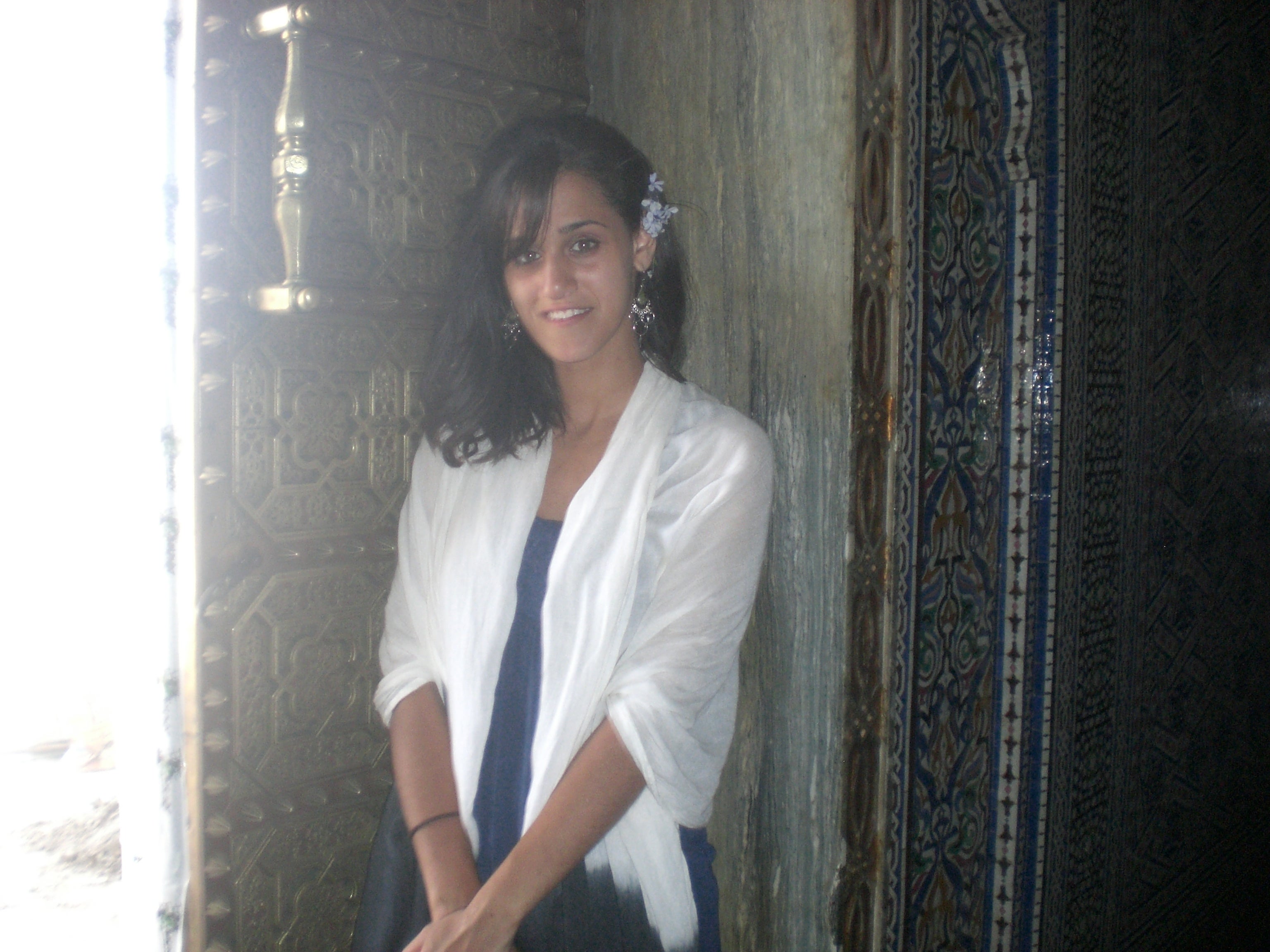 Person som står ved en utsmykket døråpning, iført et sjal over en kjole, med tilbehør til blomsterhår