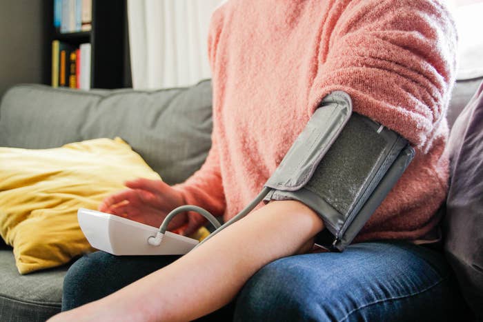 Person som sitter på en sofa med en blodtrykksmonitor på armen, fremmer helsebevissthet og egenomsorg hjemme