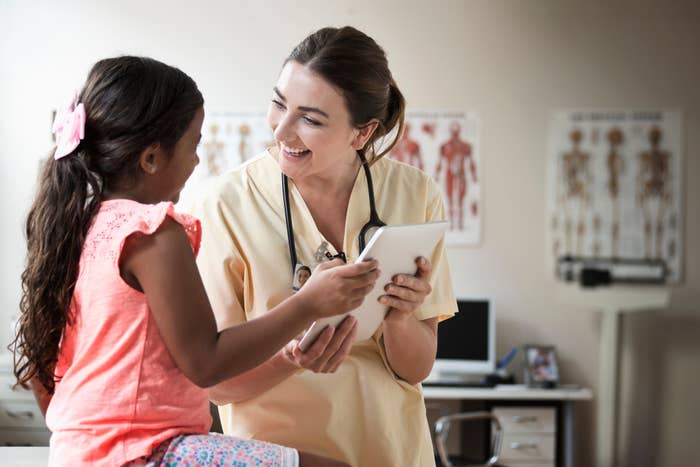 En lege i skrubber snakker gledelig med en ung jente som sitter på et eksamensbord og holder et bord