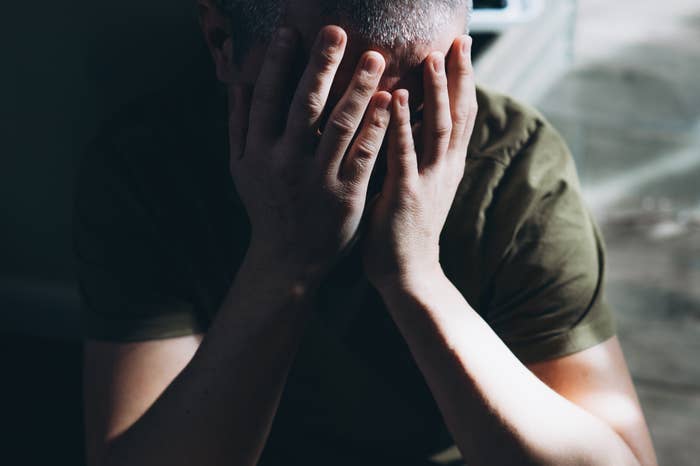 Person som sitter med hodet i hendene, virker opprørt eller stresset. De har på seg en uformell t-skjorte. Bakgrunnen er svakt opplyst
