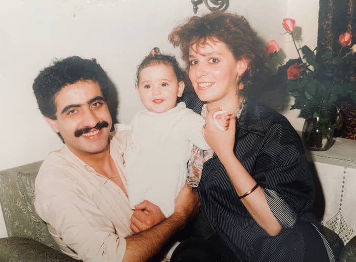 Et smilende par holder en baby mellom seg og sitter på en sofa med roser i bakgrunnen