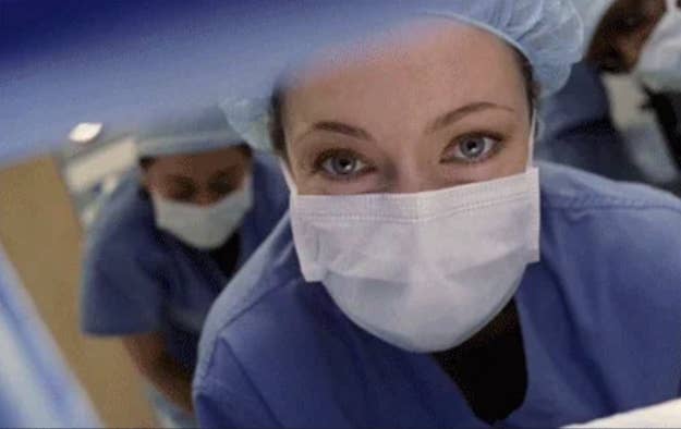 Helsetjenester i kirurgiske skrubber og masker lener seg, som om de utfører en prosedyre eller undersøker noe nøye