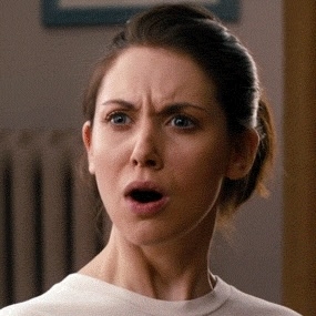 En overrasket kvinne med håret bundet tilbake, iført en topp, ser på siden med munnen åpen i sjokk