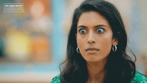 Person med brede øyne og åpen munn, som fremstår overrasket eller sjokkert. De er innendørs, iført øreringer og en mønstret topp