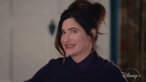 Personen smiler og trekker på en leken måte, iført et uformelt antrekk. Disney+ logo synlig i hjørnet