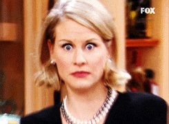 En overrasket kvinne med brede øyne og litt åpen munn, som står innendørs, og kaster seg på noe utenfor kameraet