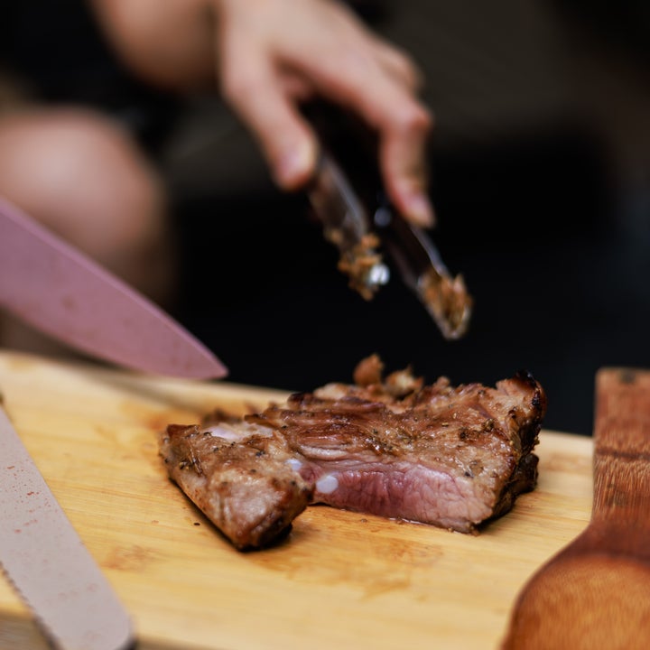 Person som skiver en kokt biff på et skjærebrett med kniv og tang. En treskje er i nærheten