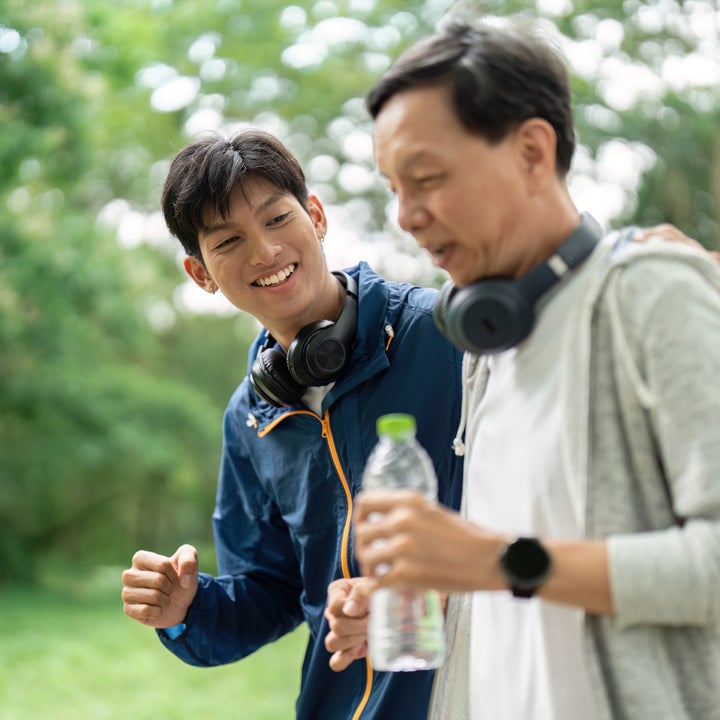 To personer med hodetelefoner, som går i en park; Den ene holder en vannflaske. Begge er tilfeldig kledd og smilende, noe som antyder glede og kameraderi