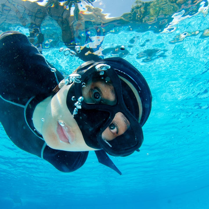 Person snorkling under vann, iført maske og snorkle. Bobler omgir dem når de ser mot kameraet