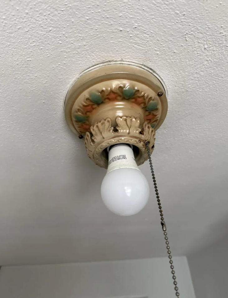 Utsmykkede vintage taklysarmatur med en synlig pære og trekkkjede. Dekorative detaljer inkluderer blomstermotiver