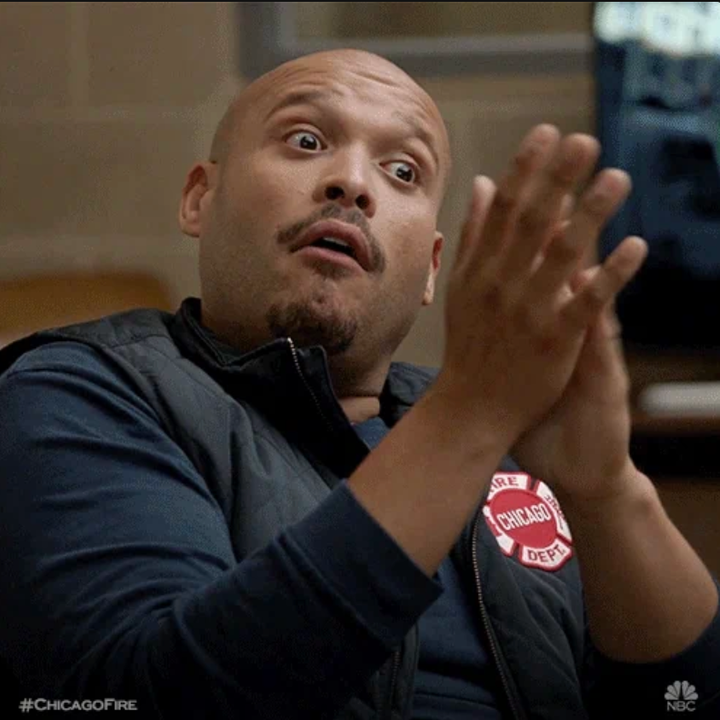 Person med overrasket uttrykk, iført en svart vest med en "Chicago Fire Dept" -lapp, i en scene fra et TV -show. Hashtag synlig: #chicagofire