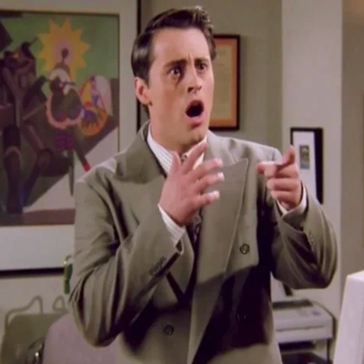 Person i dress med et forbauset uttrykk og en hånd peker, som står foran kontorlignende dekor