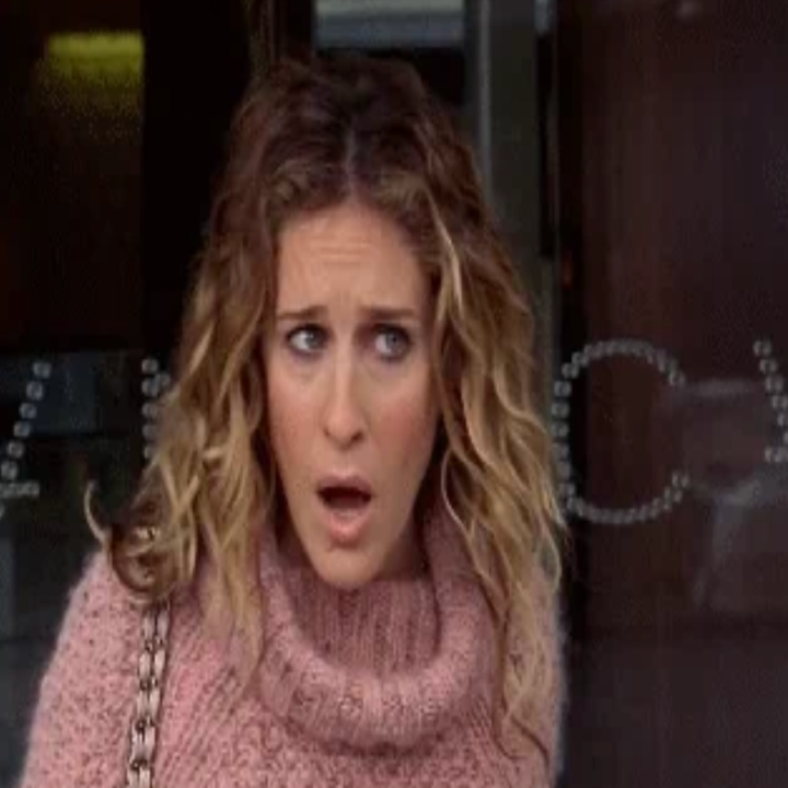 Person med krøllete hår og et uttrykksfullt ansikt har på seg en koselig strikket genser, og holder en kjedestropppose, som står utenfor med et overrasket uttrykk