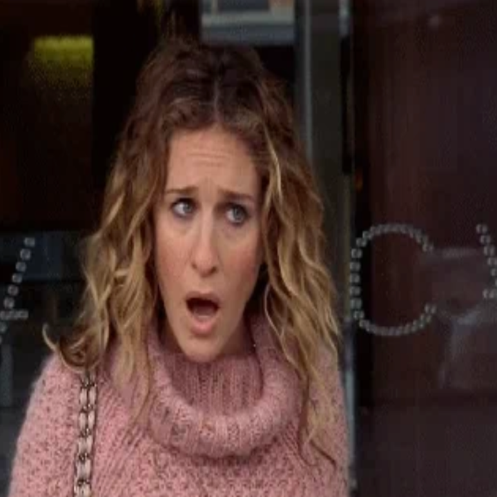 En overrasket kvinne med krøllete hår iført en koselig strikket turtleneck -genser, stående innendørs