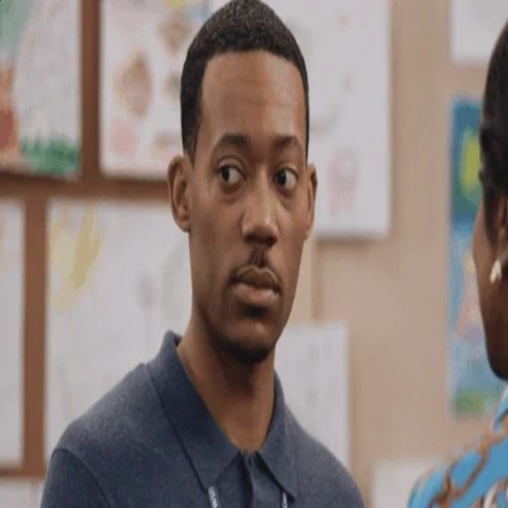 En person i en blå polo -skjorte ser noe skeptisk ut mens han står foran en vegg med forskjellige tegninger