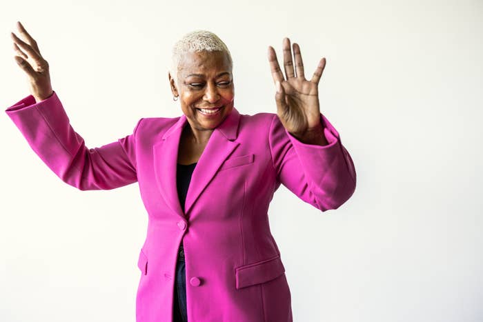 Person med glede dans, iført en stilig dressjakke, med armer hevet mot en vanlig bakgrunn