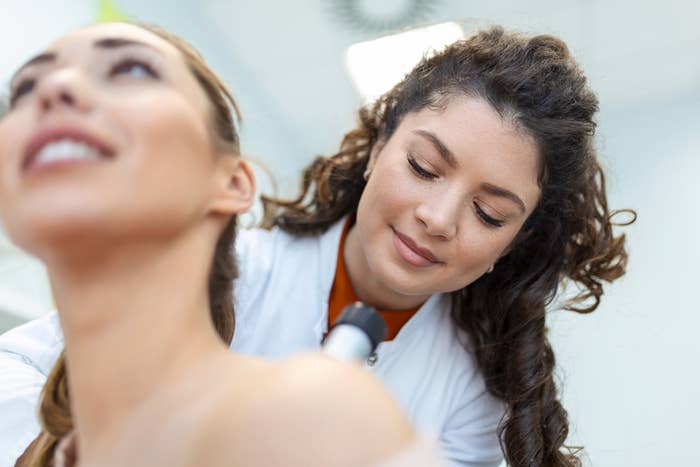 En kvinne mottar en skulderbehandling fra en smilende tekniker ved hjelp av en håndholdt enhet i profesjonell setting