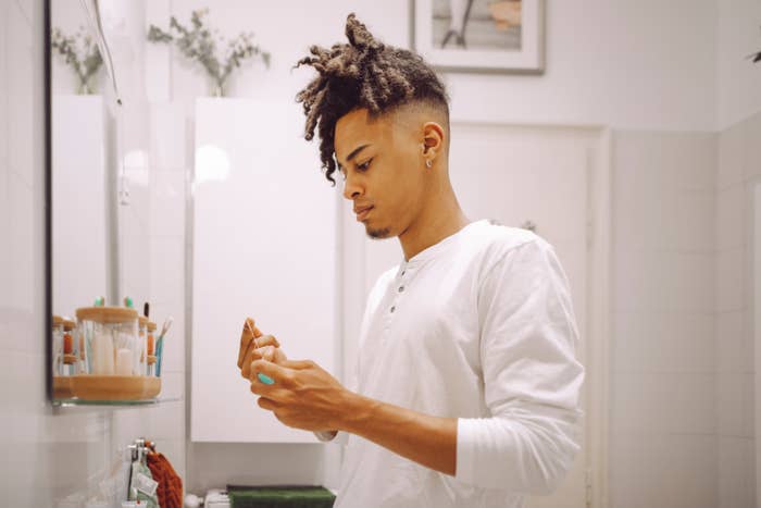 Person med stilig hår undersøker pleieprodukt på badet