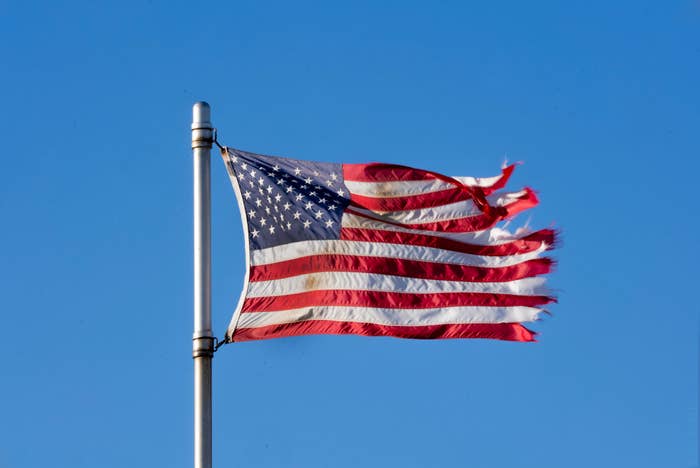 Slitt amerikansk flagg på en stolpe bølger mot en klar himmel, symboliserer spenst