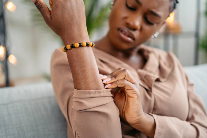 Person som sitter på en sofa, klør seg i armen, har på seg et perlet armbånd og en uformell, langermet topp