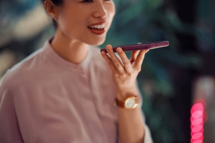 Person som holder en smarttelefon og snakker inn i den, ser ut til å bruke talekommando eller spiller inn en melding