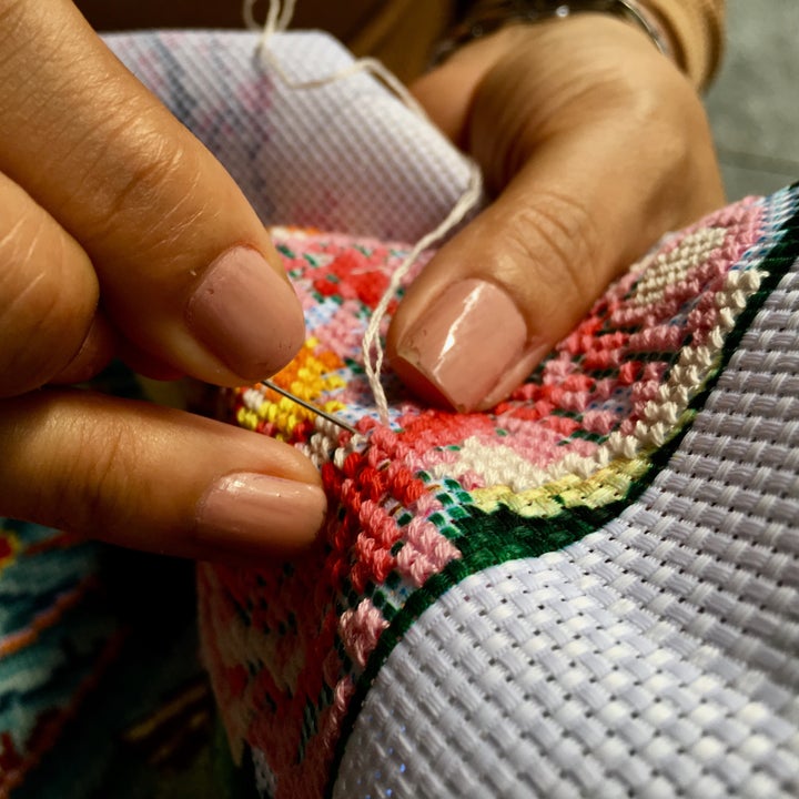 Nærbilde av hender som forsiktig broderer fargerike mønstre på stoff