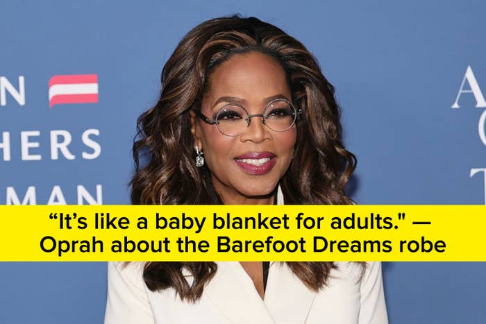 Person i en stilig hvit blazer, smilende på et arrangement med blått bakteppe med tekst og logo