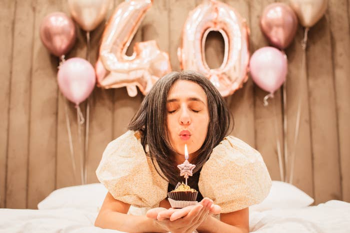 Person i en puff-ermet kjole som blåser ut et stearinlys på en cupcake, med store 