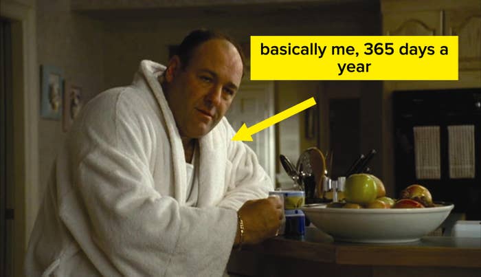 Person i badekåpe lent på en kjøkkenbenk med en kopp, nær en skål med frukt