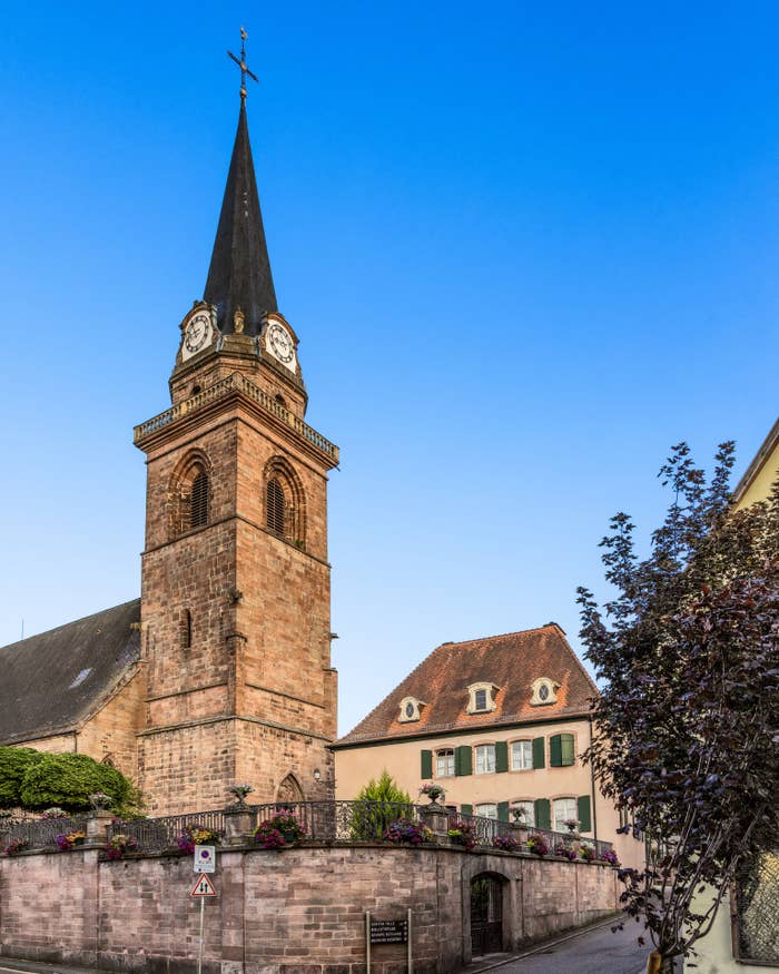 En historisk steinkirke med et høyt spir har utsikt over en sjarmerende landsbygate med sjarmerende, tradisjonelle hus