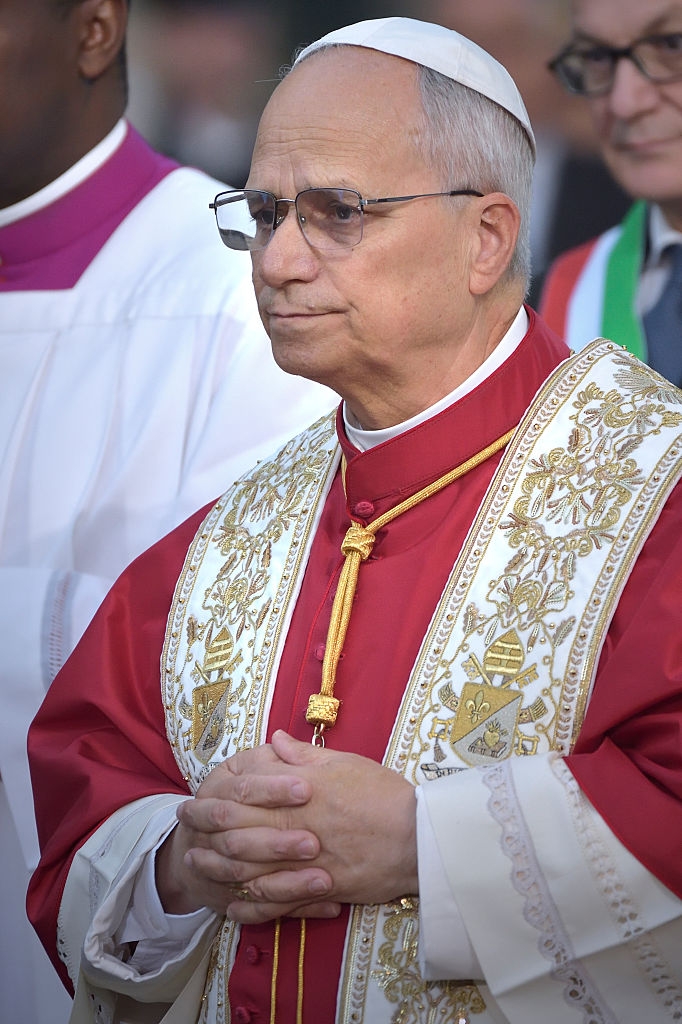 En mann i en seremoniell kappe med gullbroderi står med foldede hender og ser ut til å være i en formell eller religiøs begivenhet