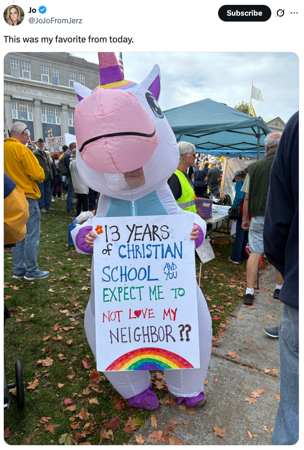 Person i et oppblåsbart enhjørningskostyme holder et skilt med teksten 
