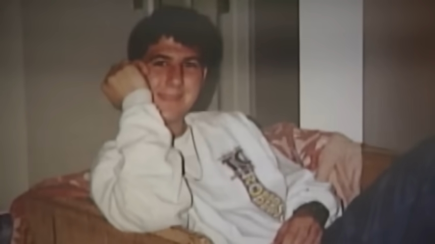 En person sitter på en sofa og smiler med en hånd på ansiktet. De har på seg en uformell genser