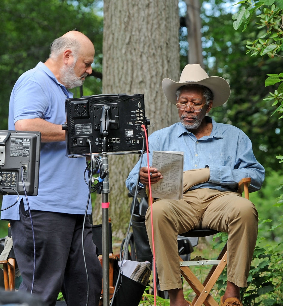 To personer på et filmsett: den ene i uformelt utendørsantrekk holder en avis, den andre står i nærheten med utstyr