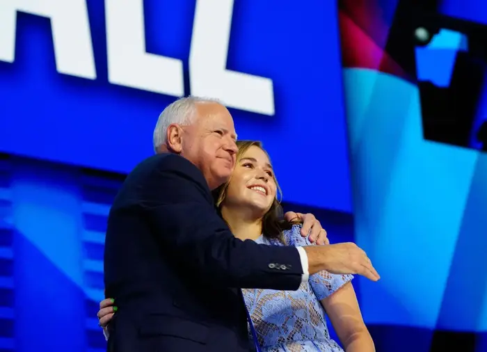 Mann og kvinne omfavner på scenen, smilende, med stor skjerm i bakgrunnen