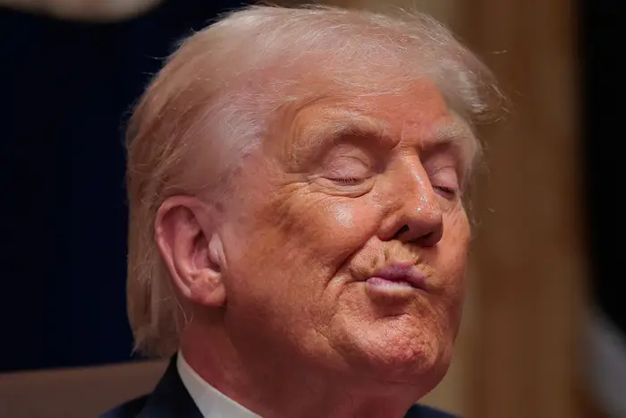 En person i dress og slips, lukkede øyne, i en gjennomtenkt eller reflekterende positur, sittende innendørs