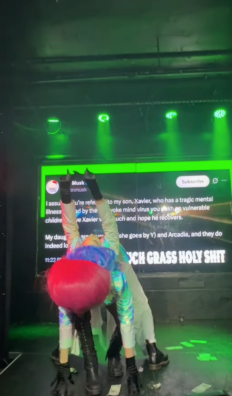 Person i futuristisk antrekk bøyd på scenen med en stor skjerm i bakgrunnen som viser tekst om en familie og personlige kamper