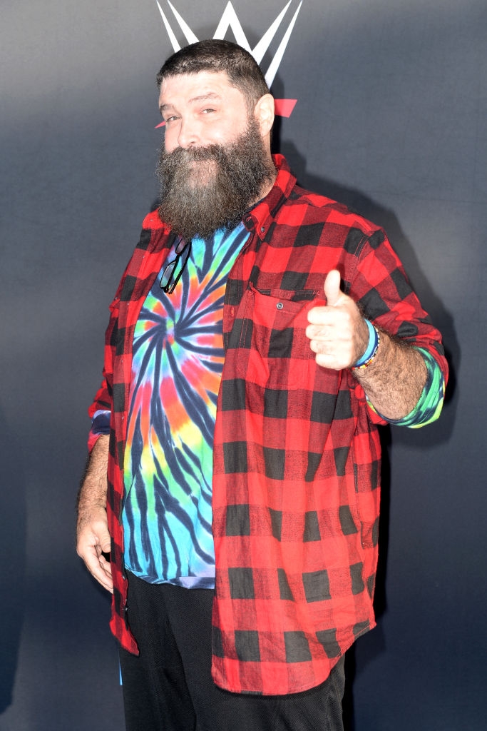 Kjendis gir tommel opp på den røde løperen, iført en tie-dye skjorte under en rød rutete jakke