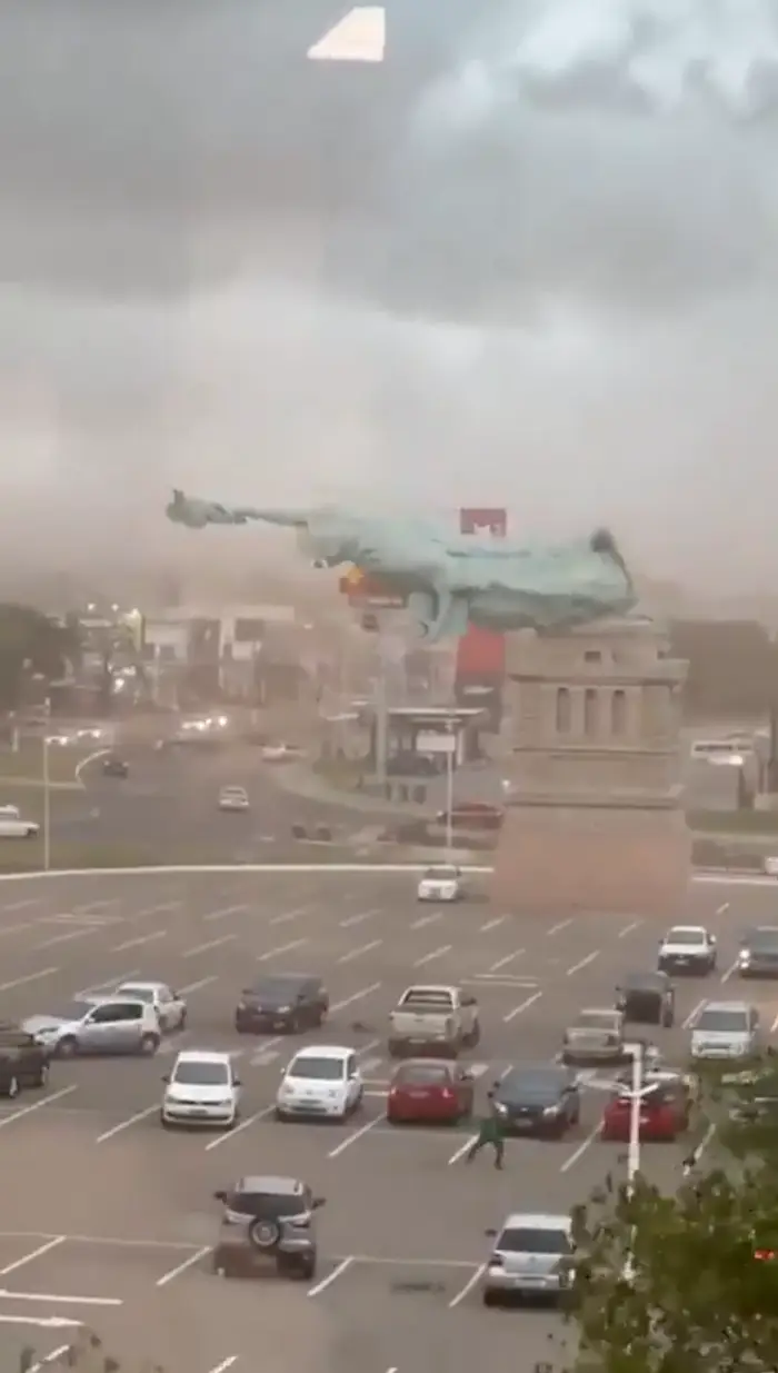 Parkeringsplass med tunge stormskyer i det fjerne og en statue som ser ut til å bli feid av sterk vind