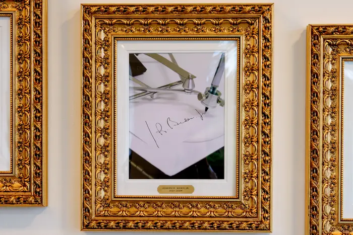 Et innrammet bilde av en maskin som simulerer en signatur, vist i en utsmykket gullramme på en vegg