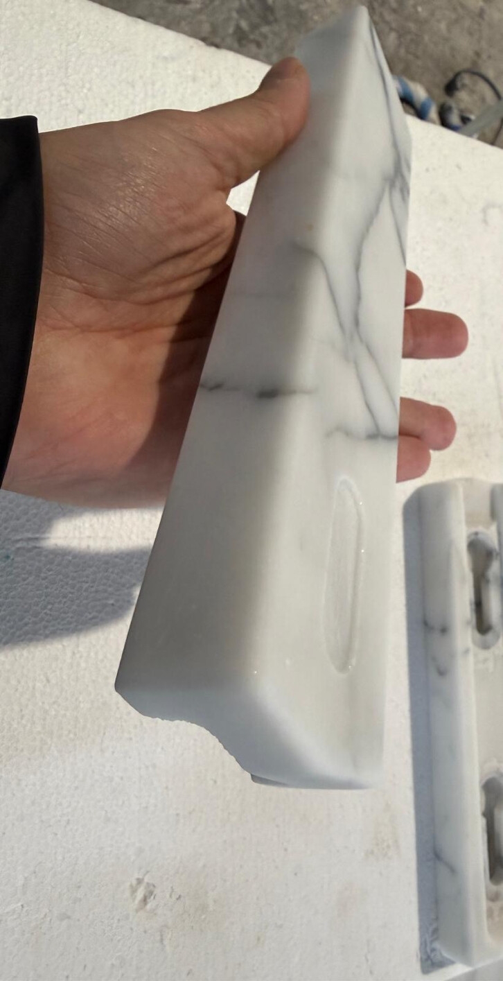 En hånd holder en marmorlignende blokk med et spor; en annen blokk er delvis synlig i bakgrunnen på en strukturert overflate