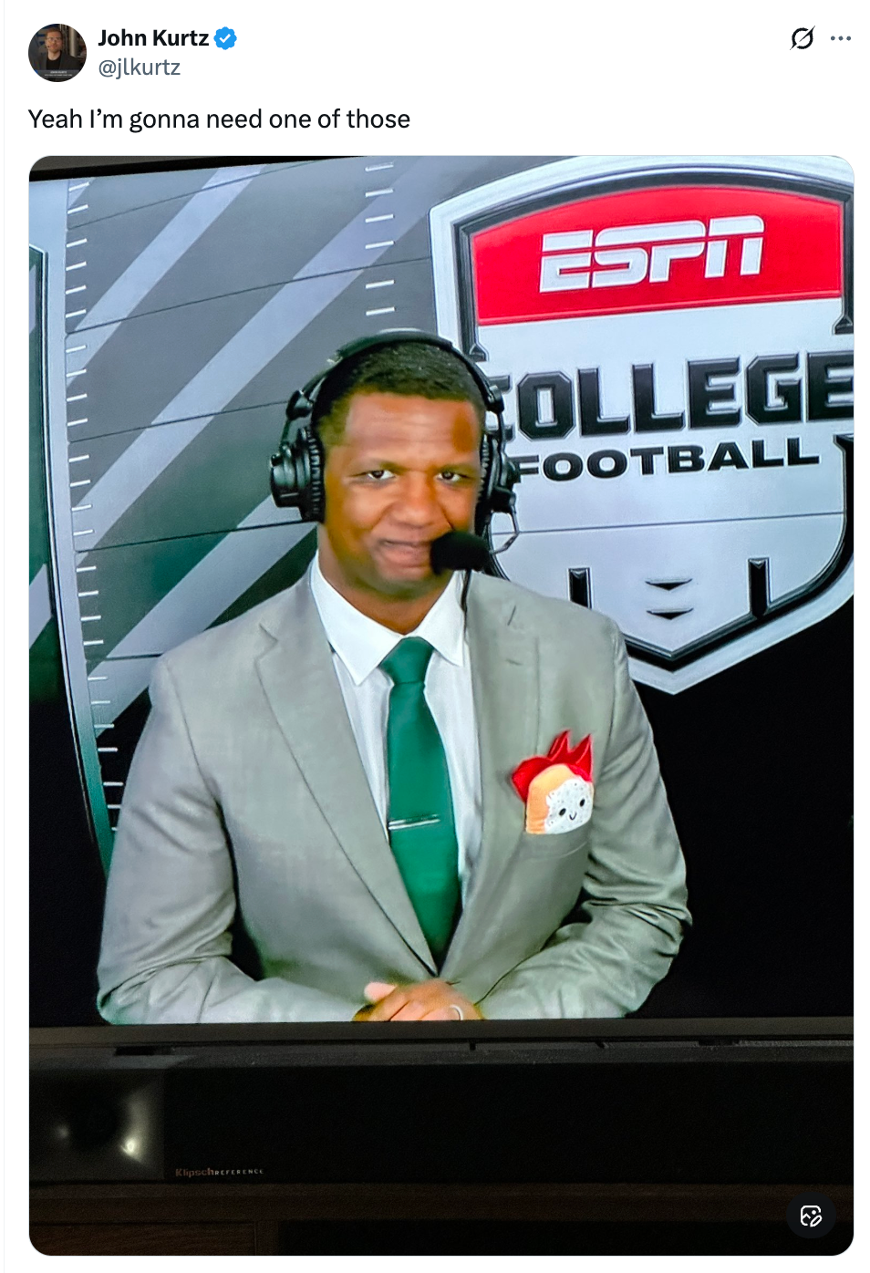 En sportskommentator i grå dress og blågrønt slips står foran et ESPN College Football-bakgrunn med et hodesett på