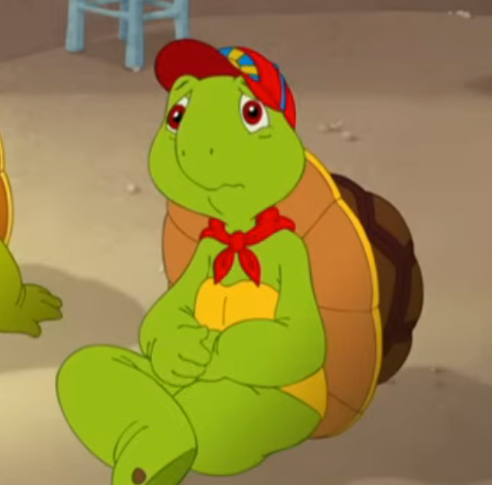 Tegneserieskilpadde iført et rødt skjerf og en fargerik lue, sitter med et bekymret uttrykk i et rom