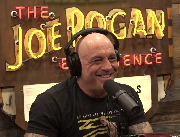 En person smiler mens han snakker i en mikrofon under et podcastopptak, med 