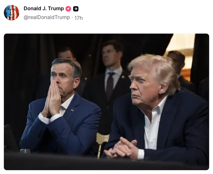 To menn sitter tett, den ene i dress med hendene knyttet nær ansiktet, den andre med armene i kors, begge virker fokuserte og lytter oppmerksomt