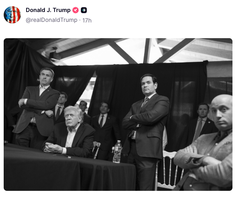 Folk sitter og står med alvorlige uttrykk på et arrangement; en person sitter ved et bord med en vannflaske